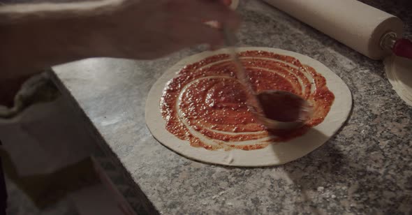 Crop chef smearing tomato sauce on pizza