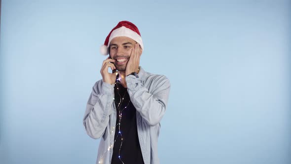 Young Happy Emotional Man Wearing Christmas Santa Hat and Garland on Neck Standing and Talking By