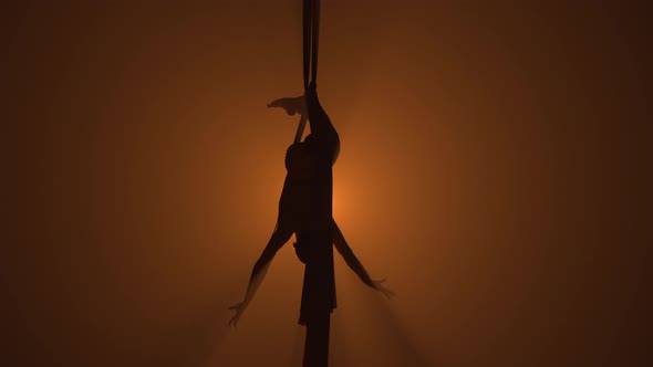 Silhouette of a Graceful Aerial Gymnast Performing Acrobatic Stunts on Aerial Silk