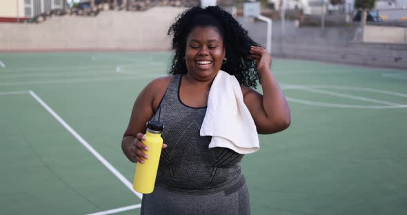 Curvy african woman smiling in camera while doing workout routine outdoor