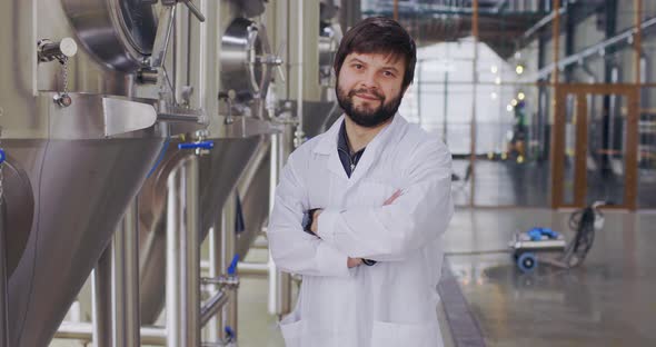 Portrait of Young Man Technologist in Lab Coat with Arms Crossed Posing at Camera in Brewery Plant