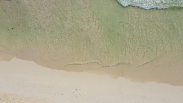 Drone journey aerial shot over a tropical beach with progressively greener and deeper crystal clear
