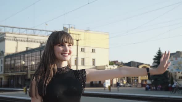 Elegant Lady Stands with Suitcase on Platform and Reach Hand Out To Sun Rays