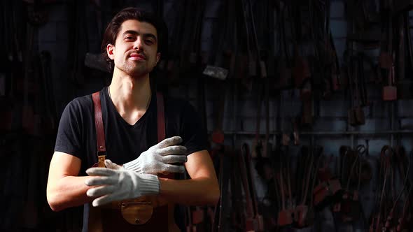 Authentic Blacksmith Man Forges a Metal Product Looking at the Camera and Arms Crossed in Dark