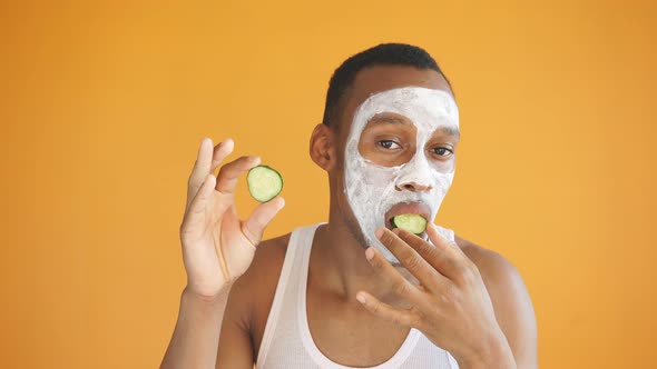 Positive African American Applies a White Face Mask with Cucumber Slices, Expresses Positive