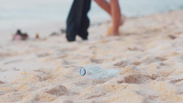 Closeup of Volunteer Picking Up Plastic Bottle on the White Ocean Beach