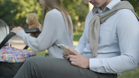 Side View of Unrecognizable Busy Man Messaging on Smartphone As Cheerful Blurred Woman Rocking Baby