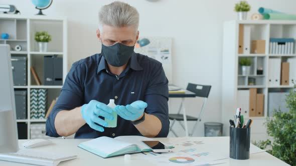 Man in Face Mask and Gloves Wet Wiping Hands with Sanitizer in Modern Office