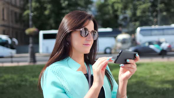 Enthusiastic Young Travel Woman in Sunglasses Using Smartphone at Sunny Cityscape Background