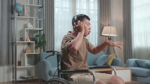 Young Asian Boy Sitting In A Wheelchair Listening To Music With Headphones And Dancing