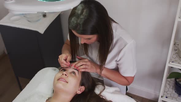 Caucasian woman wearing face mask lying down having eyebrows dyed