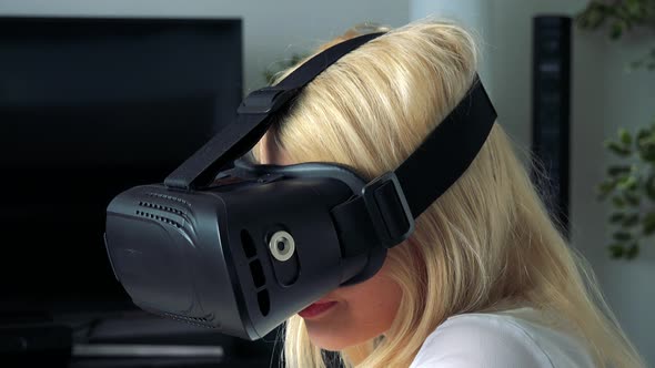 Young Attractive Blond Woman Uses Virtual Reality Glasses in Home, in Living Room - Closeup