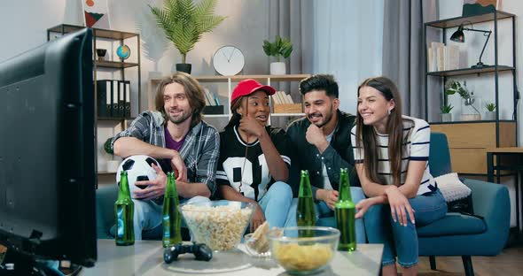 Mixed Race People Having Fun Together while Watching Sports Game on TV at Home with Snacks and beer