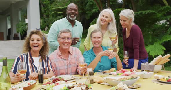 Animation of diverse happy senior female and male friends eating lunch in garden