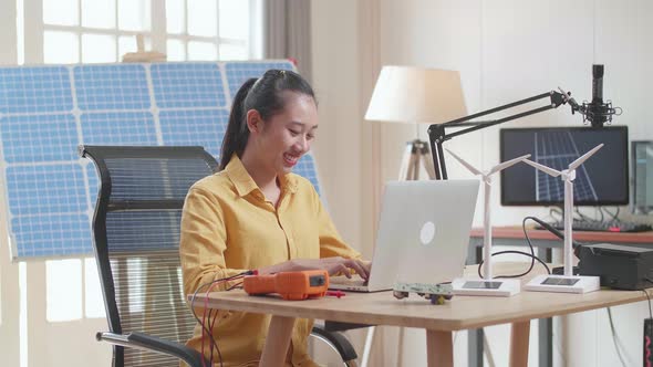 Asian Woman Sitting In Front Of Solar Cell Typing On A Laptop At The Office