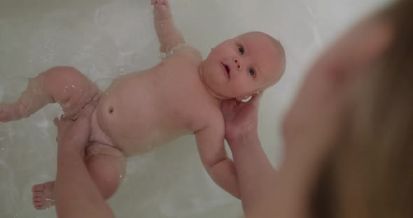 Fun View of Cute Newborn Tries to Swim on Back in the Bath with Mother Help