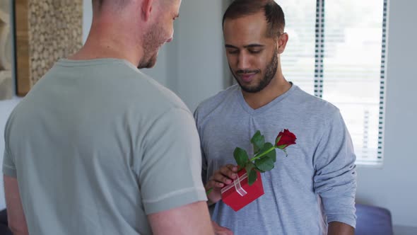 Multi ethnic gay male couple embracing one holding a gift