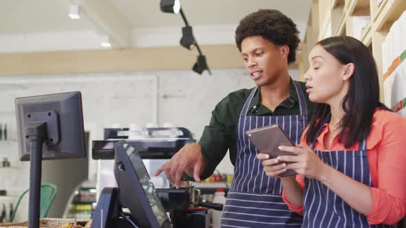 Video of happy diverse female and male waiters in aprons working with tabelet at coffee shop