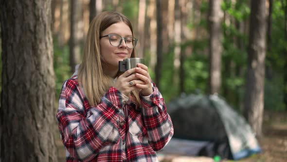 Satisfied Caucasian Young Woman Drinking Tea From Thermos Smiling Looking Around Standing in Forest