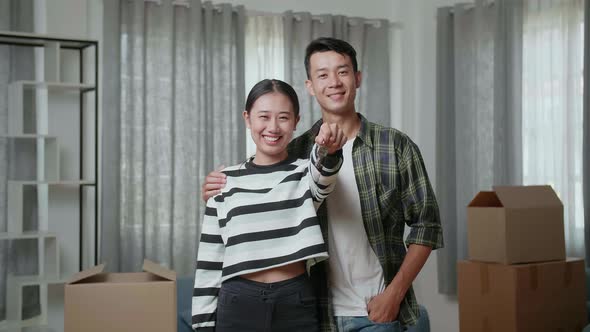 Young Asian Couple With Cardboard Boxes Smiling And Showing The Keys To Camera In The New House
