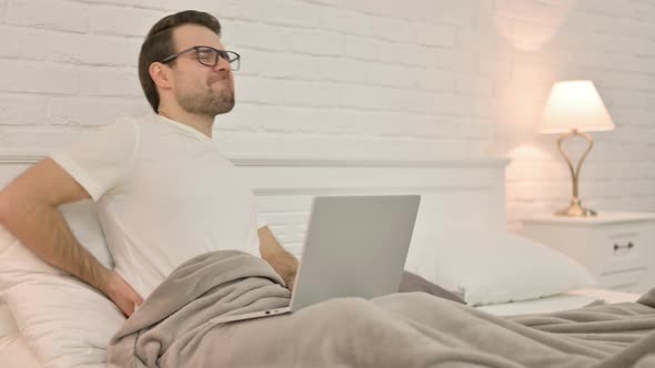 Young Man with Laptop Having Back Pain in Bed