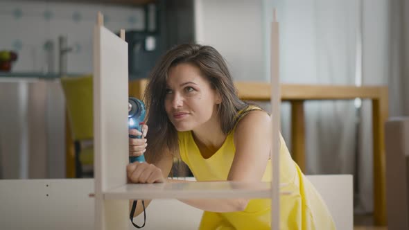 Portrait of Beautiful Young Woman Putting Together New Furniture Using Screwdriver