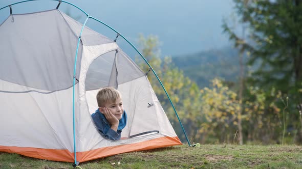 Happy Child Boy Resting in a Tourist Tent at Mountain Campsite Enjoying View of Beautiful Summer