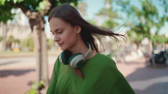 Confident blonde woman in headphones wearing green t-shirt walking