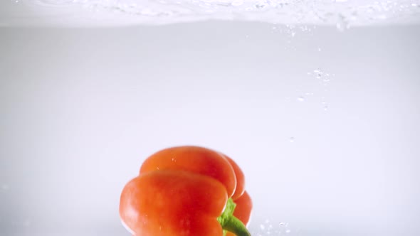 Orange Bell Pepper Falls Down in Clear Water with Bubbles