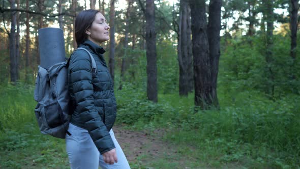 Young Woman with a Backpack Walks Through the Woods Alone