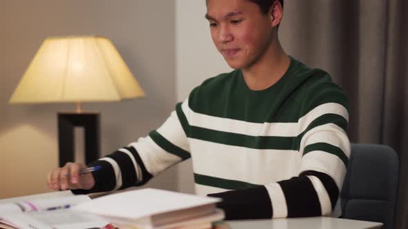 Close-up Side View of Smiling Asian Boy Writing in Workbook and Looking Into Book. Happy Teenage