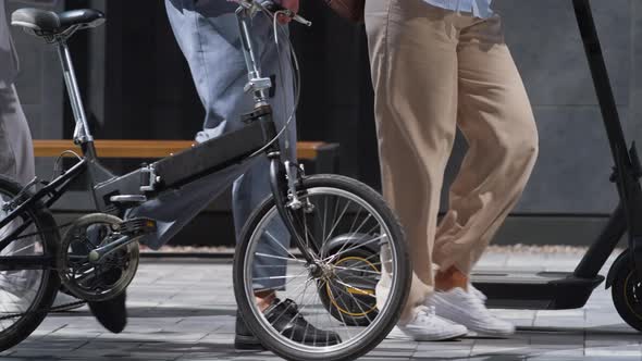 Workers Legs Walking Downtown with Electric Scooter Bicycle in Hands Close Up