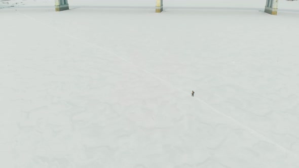 Person Silhouette Crosses White Frozen River Against Bridge