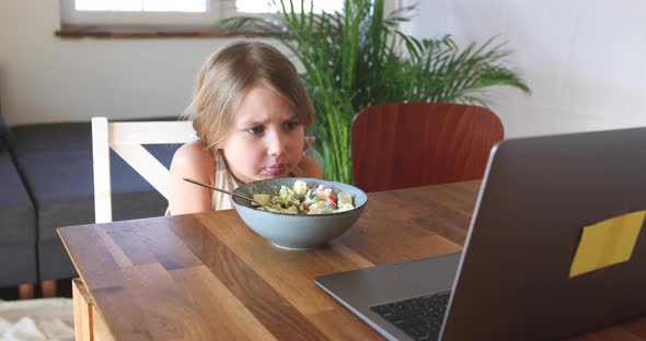 Young girl eating and watching video on laptop