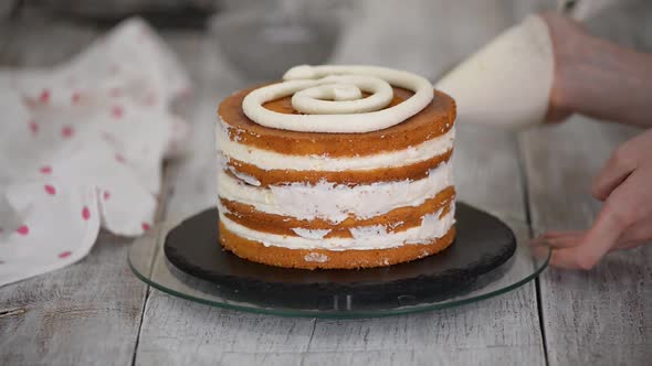 Confectioner Rotates the Cake on a Stand and Decorates with Cream From the Pastry Bag