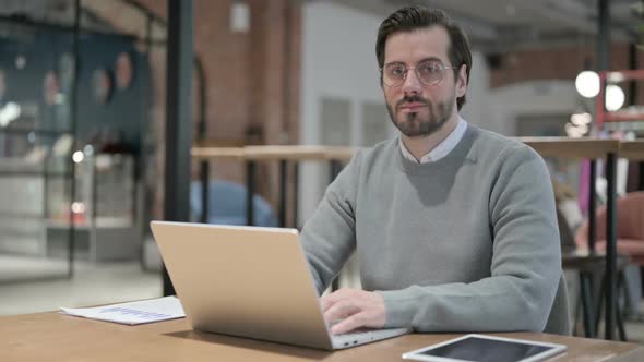 Young Man Showing Thumbs Up Sign While Using Laptop at Work