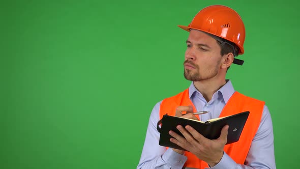 A Young Handsome Construction Worker Writes Into a Notebook - Green Screen Studio