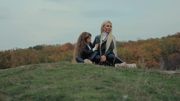 Mother with Daughter Sitting on a Ground Together at the Fall
