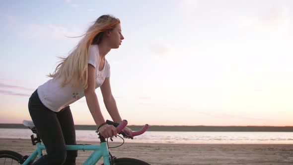 Young Attractive Woman Riding Biycle on the Beach Near the Sea During Sunrise or Sunset Slow Motion