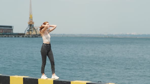 Young Stylish Funky Red Haired Woman Walking Near Sea Port During Sunny Day and Enjoys the Moment