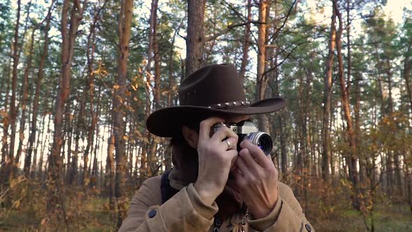 A Man in a Hat Takes Pictures in the Forest