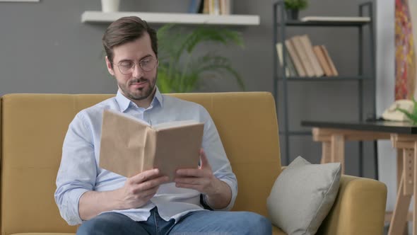 Young Man Reading Book While Sitting on Sofa