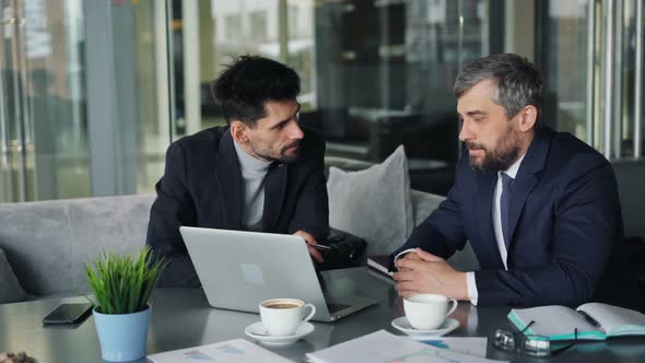 Business Partners Negotiating Contract Talking Looking at Laptop Screen in Cafe