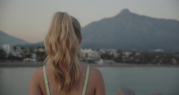 Woman Walking In Sunset Along Promenade By Sea