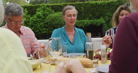 Animation of happy diverse female and male senior friends having lunch in garden, praying