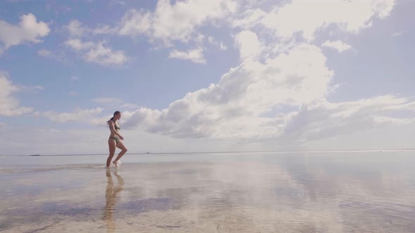 Cheerful Woman in Beach Bikini Walking on Sea Water at Shore on Blue Sky Landscape. Attractive Woman