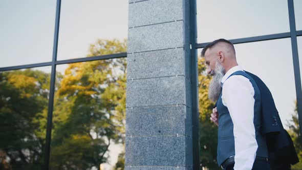 Handsome Bearded Mature Man in Suit Walking Outdoors on Modern Building Background During Sunny Day