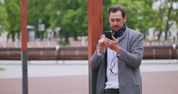 Young Man with Mustaches and a Beard with Headphones on His Neck Stays on the Wooden Floor in the