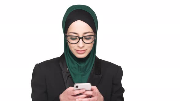 Portrait of Beautiful Arabic Woman in Headscarf Typing Text Messages on Smart Phone Isolated Over
