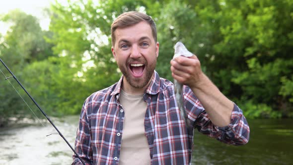 Fisherman Rests on the River and Catches Trout Smiles and Shows the Fish in the Camera